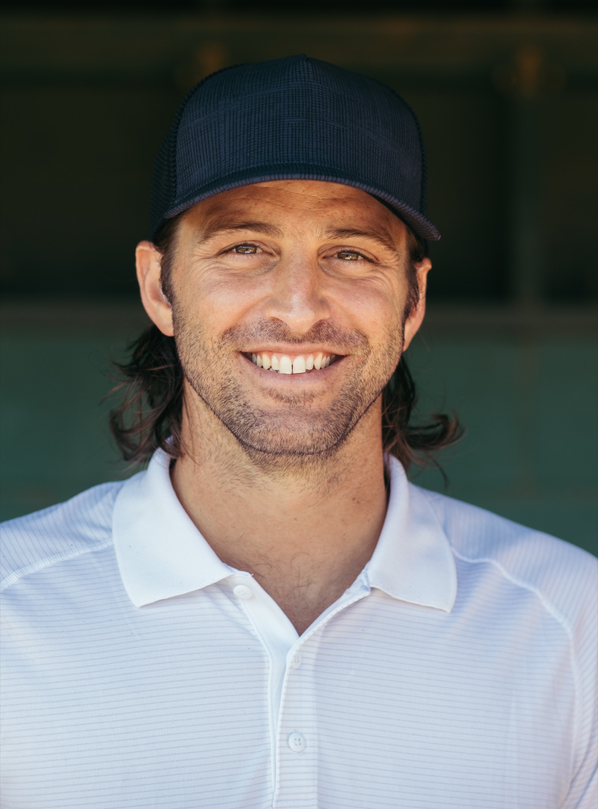 Coach Zach Penprase — ballcap, easy smile, dugout behind him